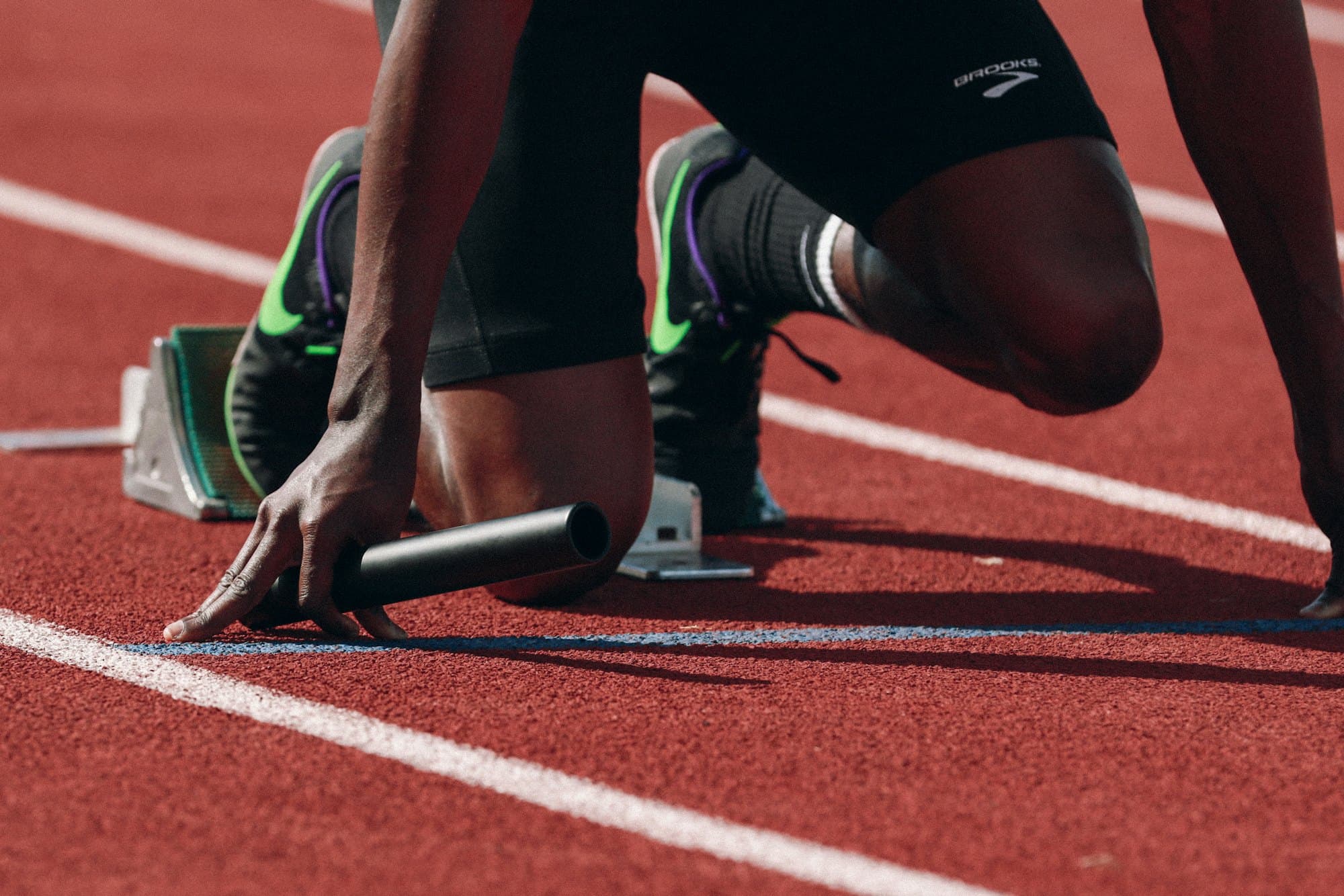 A sprinter crouched in the blocks holding a relay baton